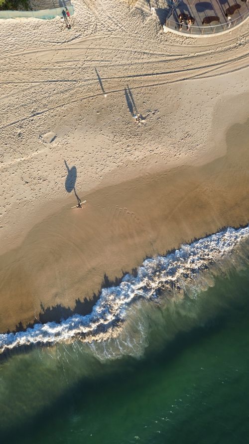 Free Aerial view of a sandy beach with a lone surfer and ocean waves during day. Stock Photo