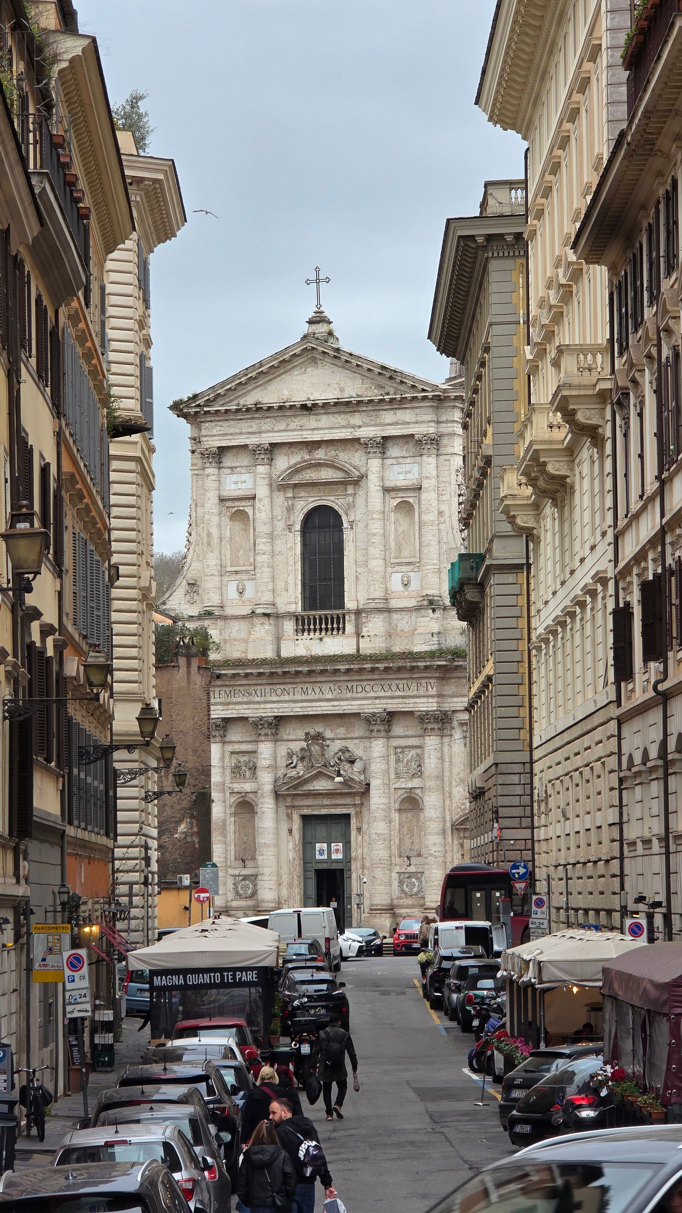 A view down a busy street in Rome leading to a historic church with classic architecture.