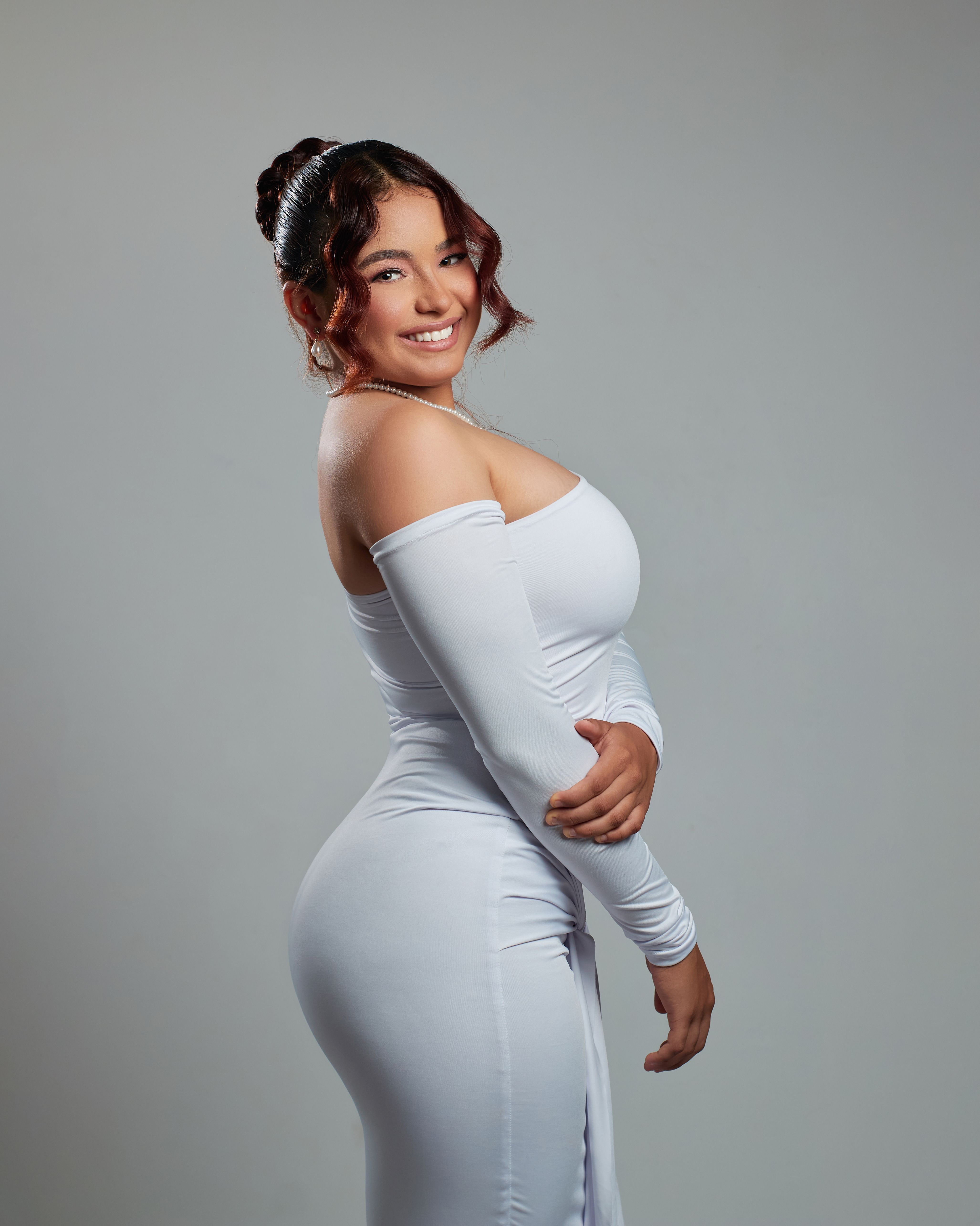 Portrait of a stylish woman in an off-shoulder white dress, smiling confidently.