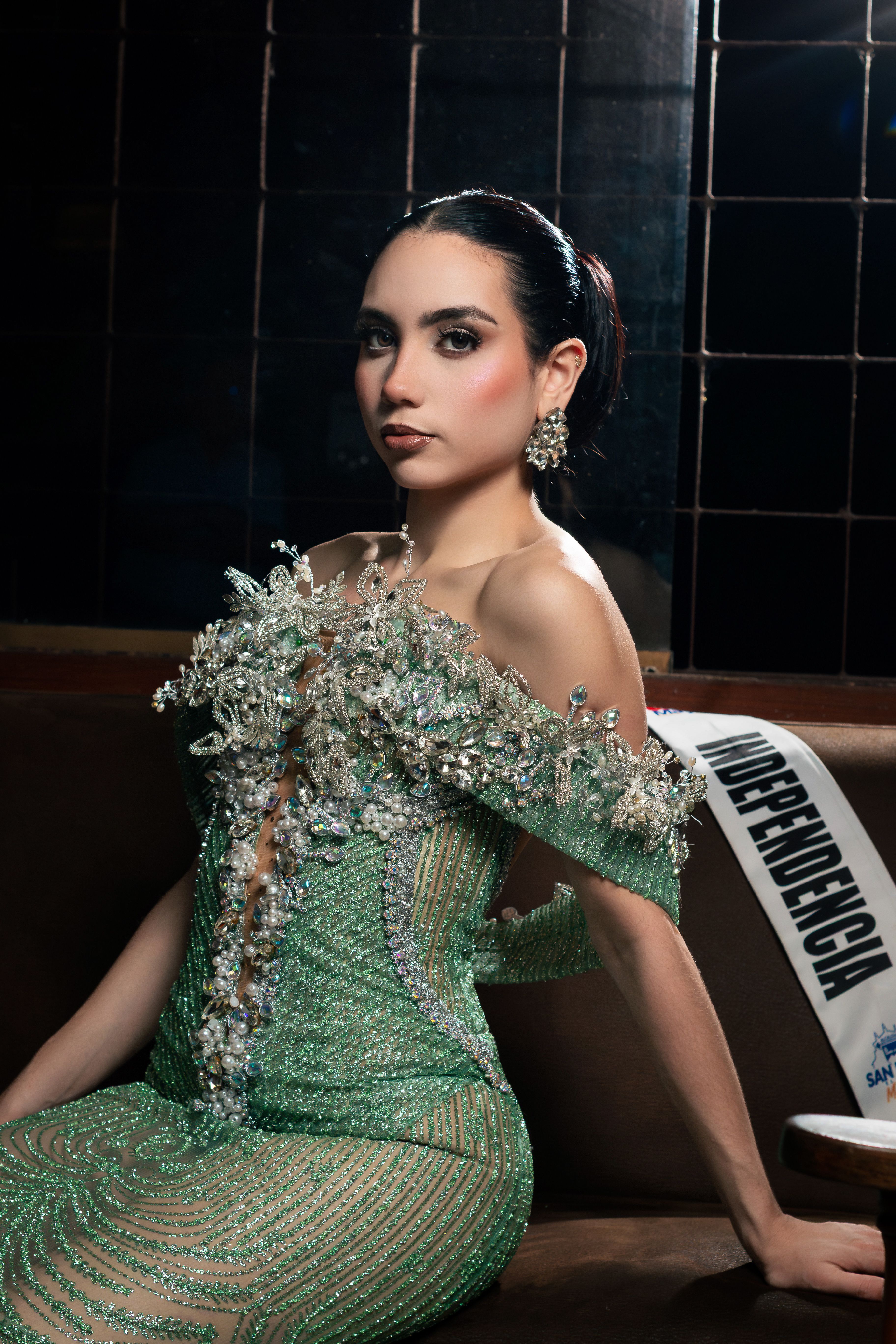 Woman posing in an elaborate green evening gown and ornate earrings indoors.