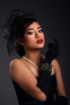 Portrait of an elegant woman in vintage attire with red lipstick and pearls, exuding glamour.