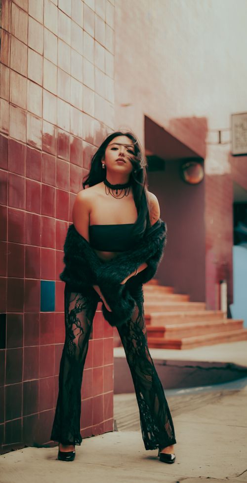 Free Striking urban fashion photoshoot featuring a woman in chic black attire against a textured wall. Stock Photo