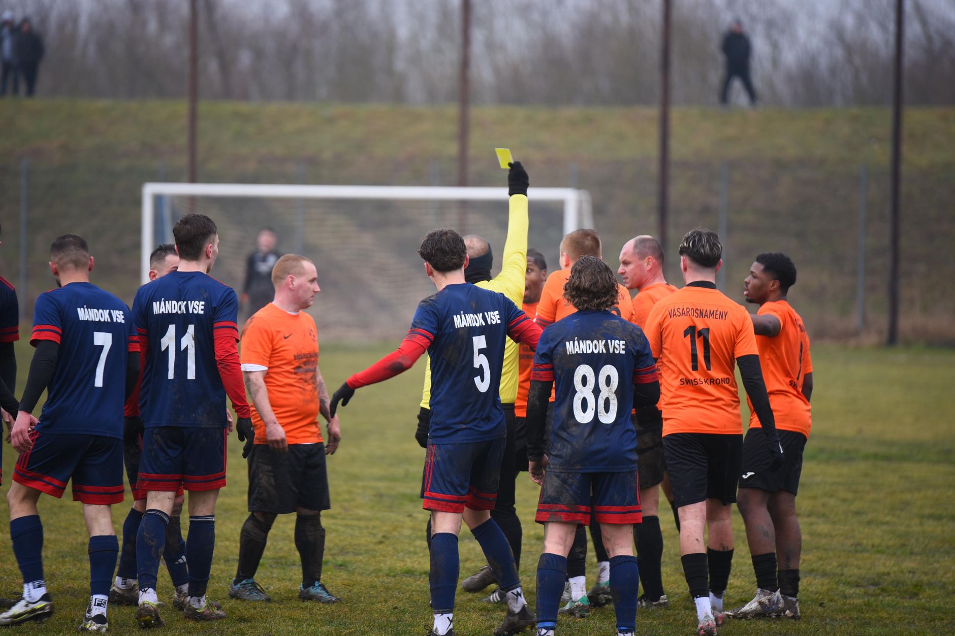 Soccer players show sportsmanship as referee issues yellow card during a match in Vásárosnamény, Hungary.