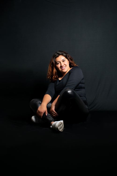 Free Studio portrait of a smiling woman in casual attire seated against a black background. Stock Photo