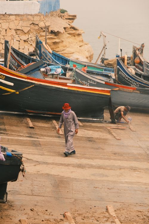Free Fishermen working around traditional fishing boats in a dusty harbor area, creating a rustic scene. Stock Photo