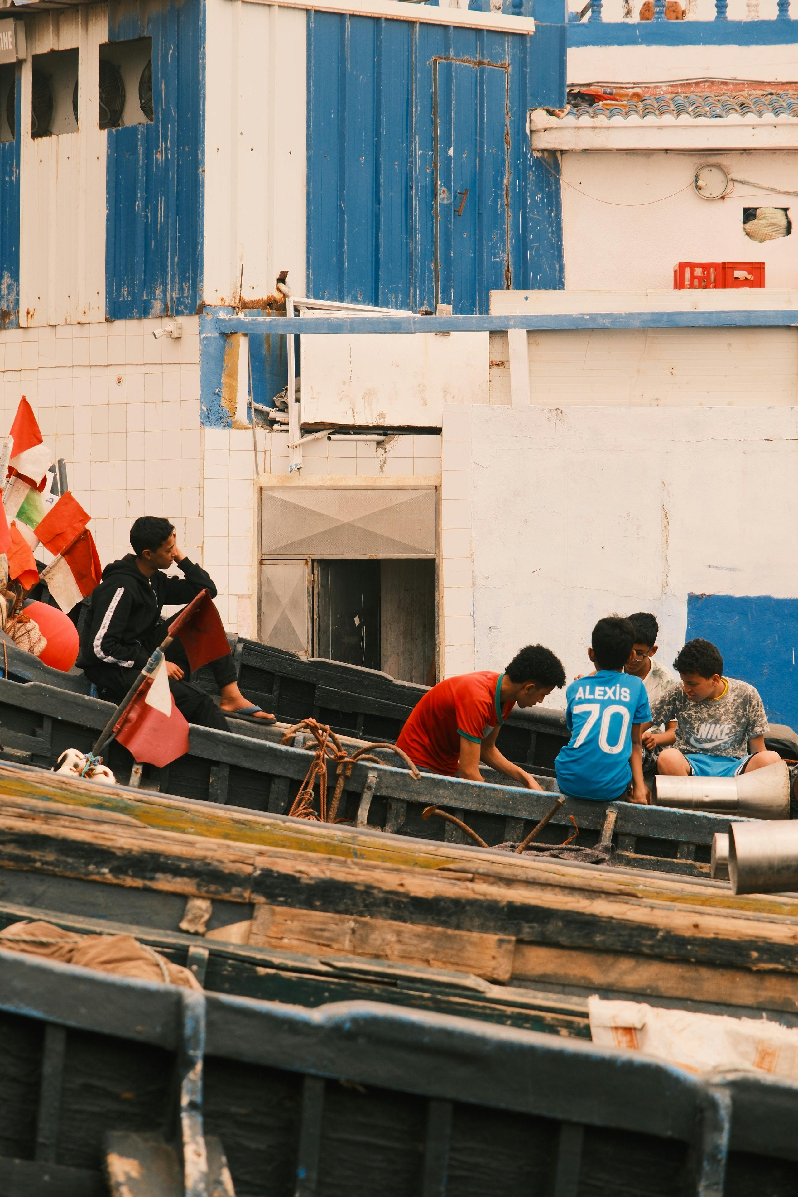 Young adults gather on docked fishing boats in a coastal setting, evoking exploration and camaraderie.