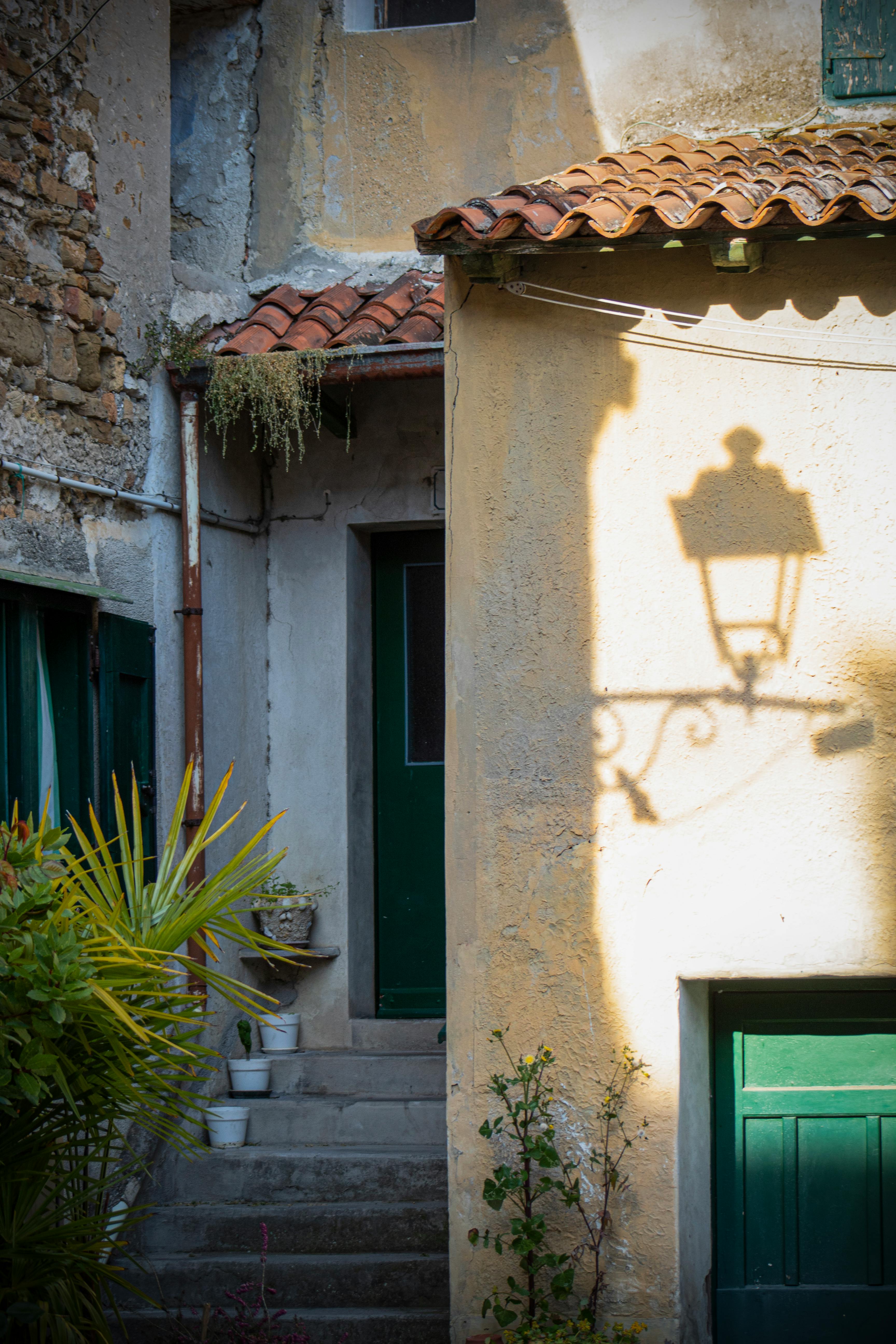 Sunlight casts a lamp shadow on a rustic building in a picturesque Grado alley.