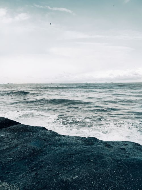 Free A calm ocean scene with gentle waves hitting the rocky shoreline under a cloudy sky. Stock Photo