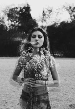 Black and white double exposure portrait of a woman holding flowers outdoors, creating a surreal artistic effect.
