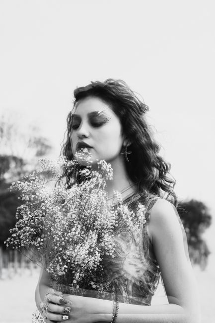 Fotomural Retrato de una mujer contemplativa sosteniendo un ramo de flores al aire libre. Capturada en blanco y negro, transmite una atmósfera tranquila y onírica.