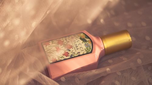 Free A close-up of a Gucci Flora perfume bottle surrounded by delicate fabric in warm lighting. Stock Photo