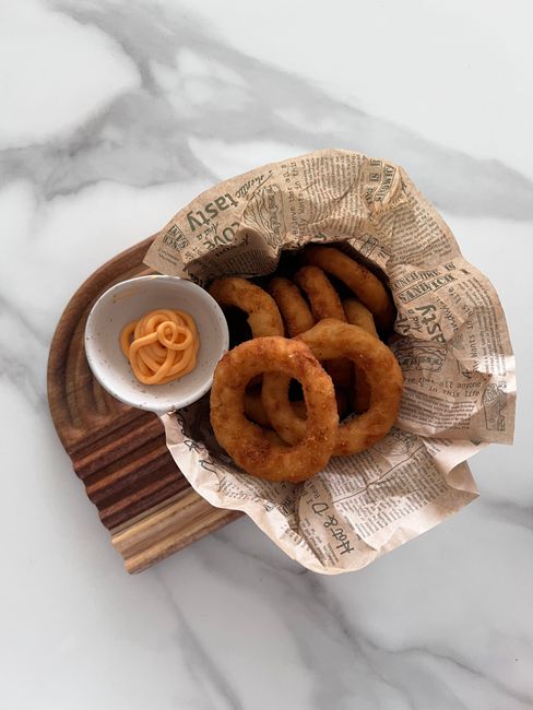 A golden, deep-fried onion cut into open petals on a plate next to a small bowl of creamy orange dipping sauce, with one petal pulled away.