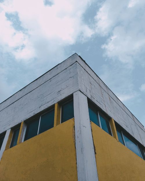 Free Corner view of a yellow and white abandoned building under a cloudy sky, modern architectural design. Stock Photo
