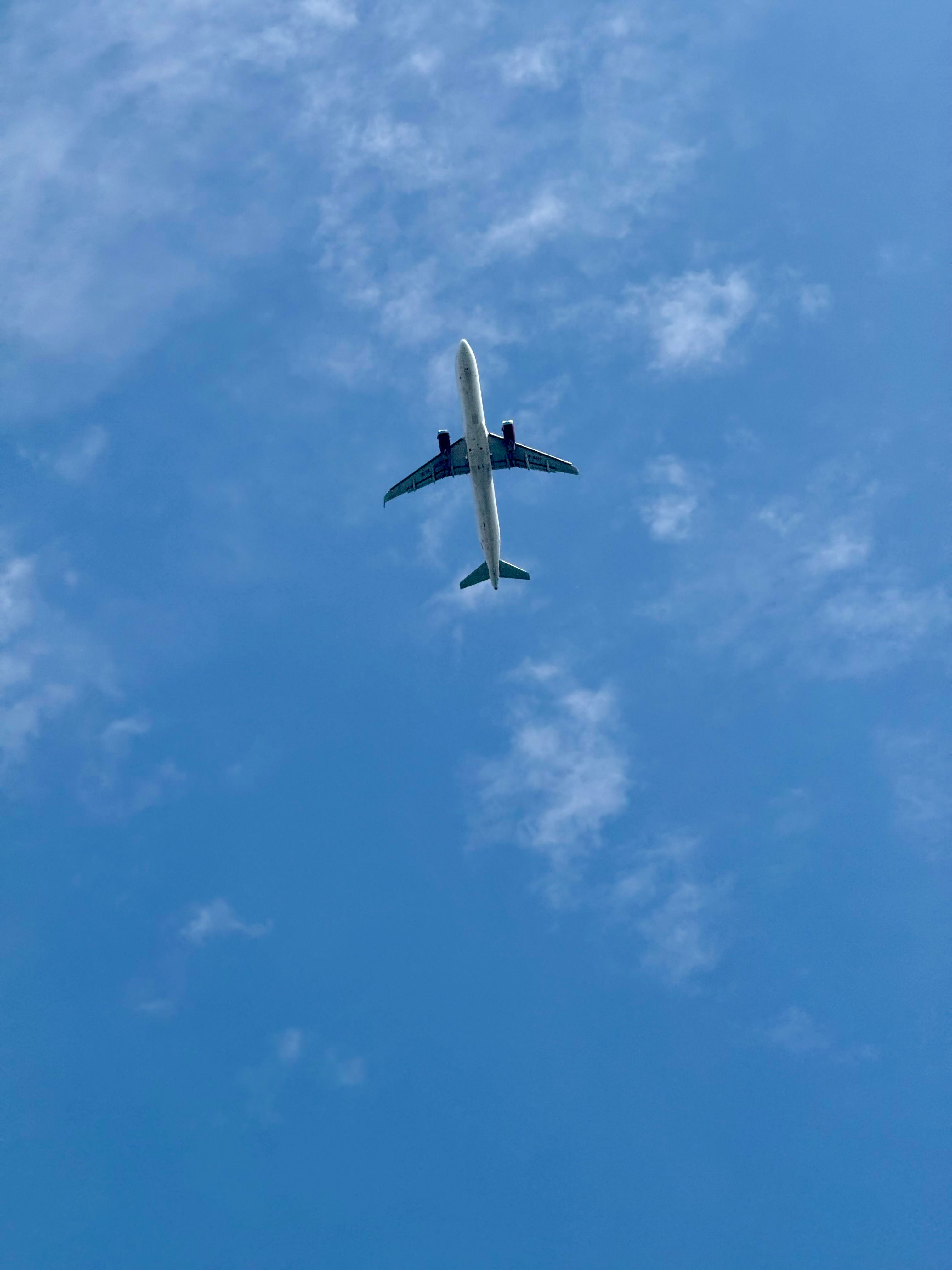 Commercial airplane flying high in a clear blue sky with scattered clouds, viewed from below.