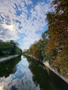 Beautiful canal in Berlin, Germany reflecting the cloudy sky and lush trees.