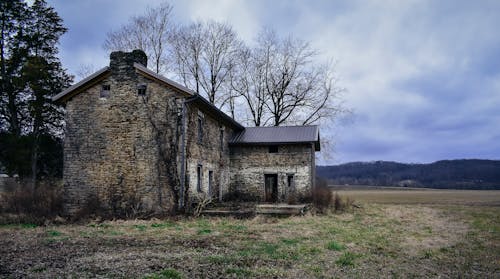 Brown Brick House Near Bare Trees Under Cloudy Sky