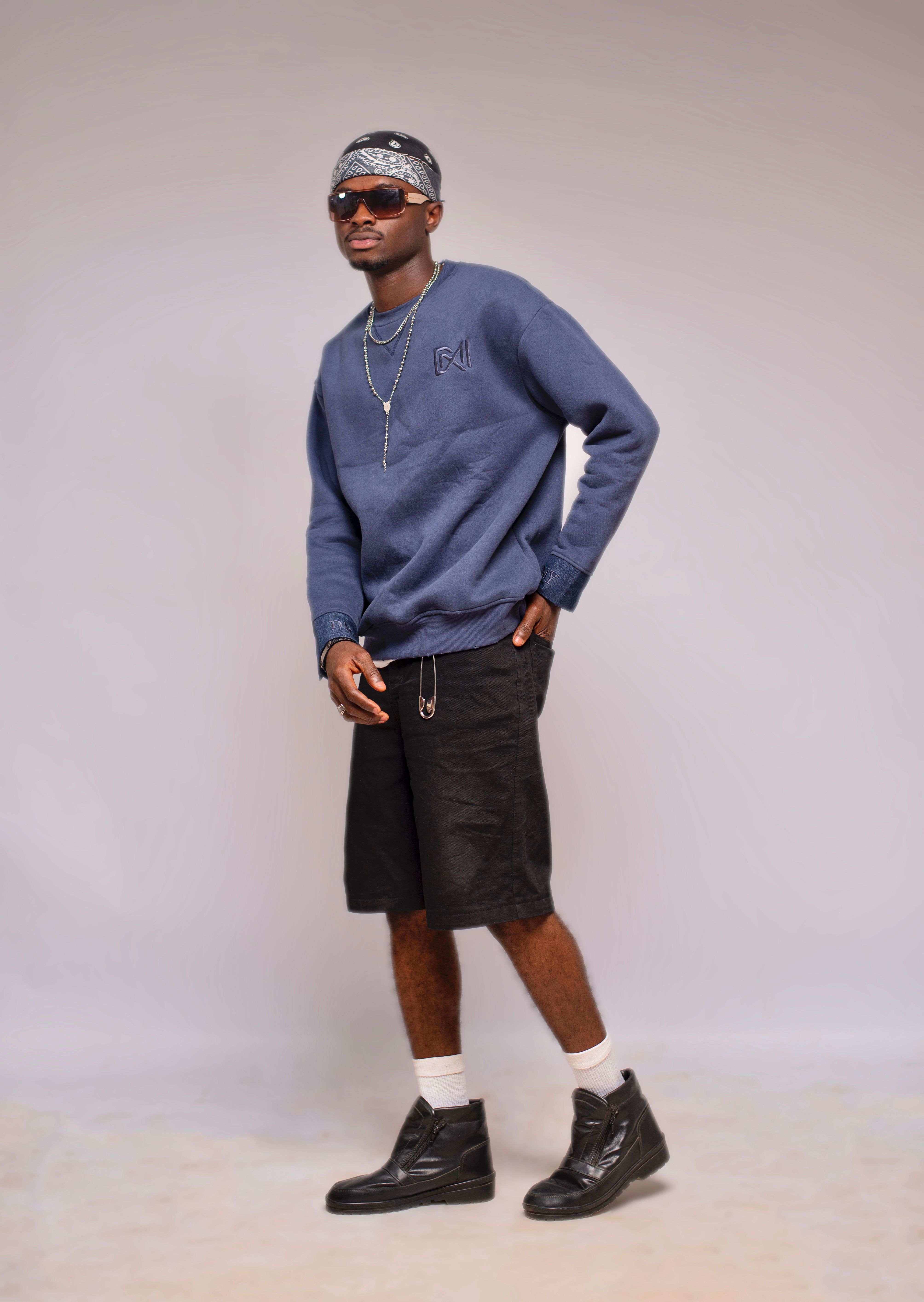 Trendy young adult wearing casual blue sweatshirt and black shorts, posing confidently indoors.