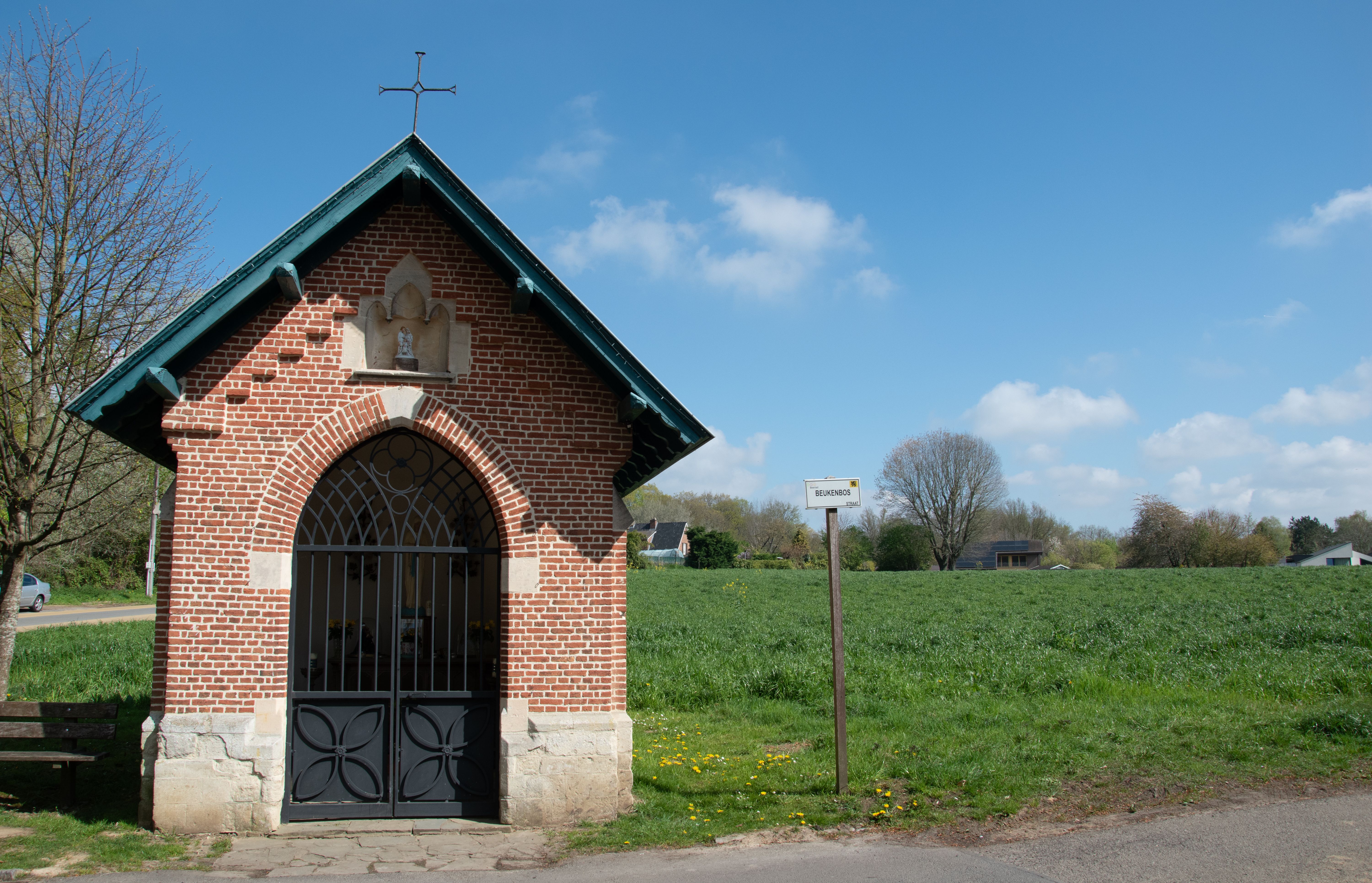A quaint brick chapel situated in the serene countryside of Beersel, Belgium, under a bright blue sky.