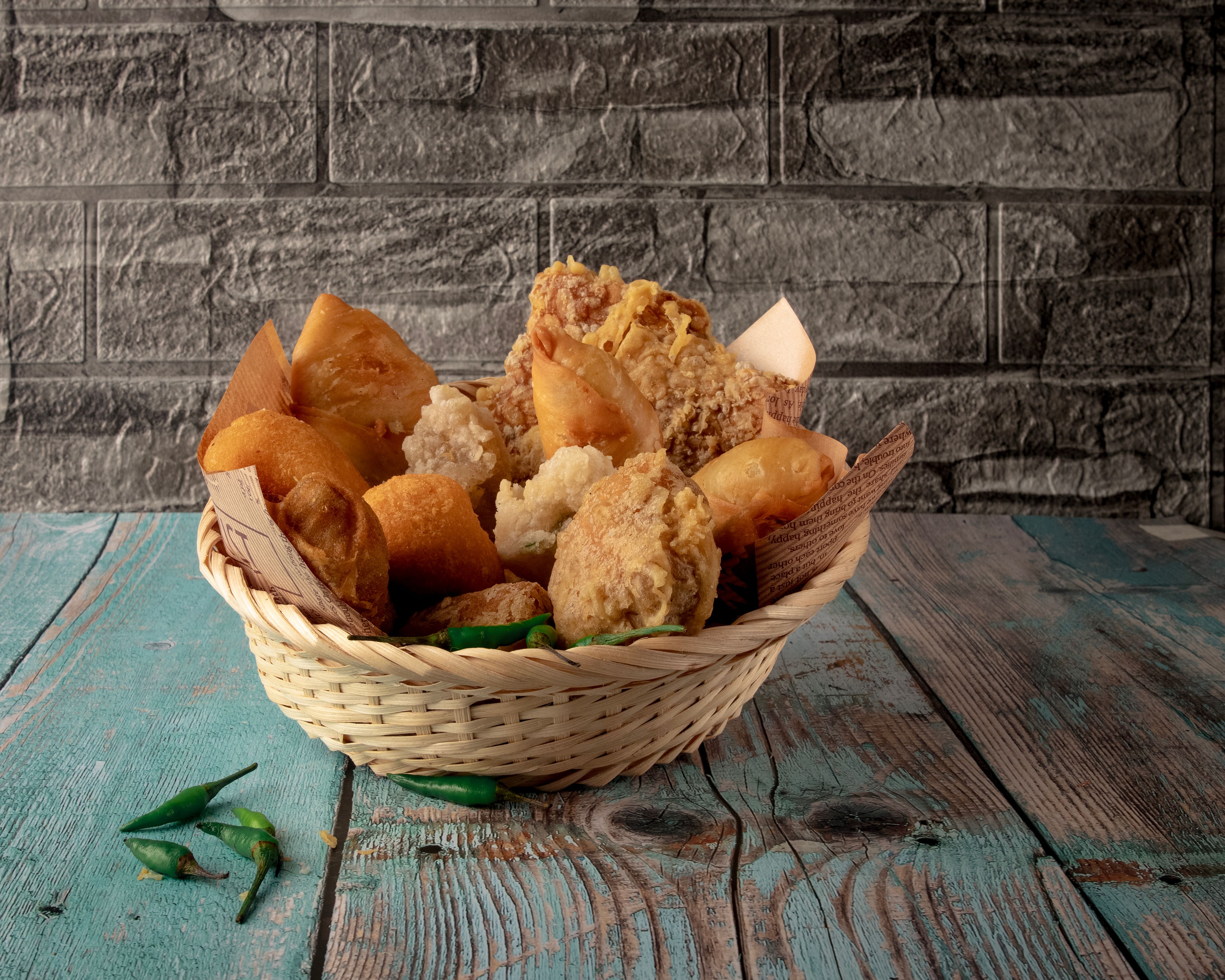 Uma cesta de pão crocante e empanado, ideal para um café da manhã ou lanche caseiro, colocada sobre uma mesa de madeira com fundo de parede de pedra.