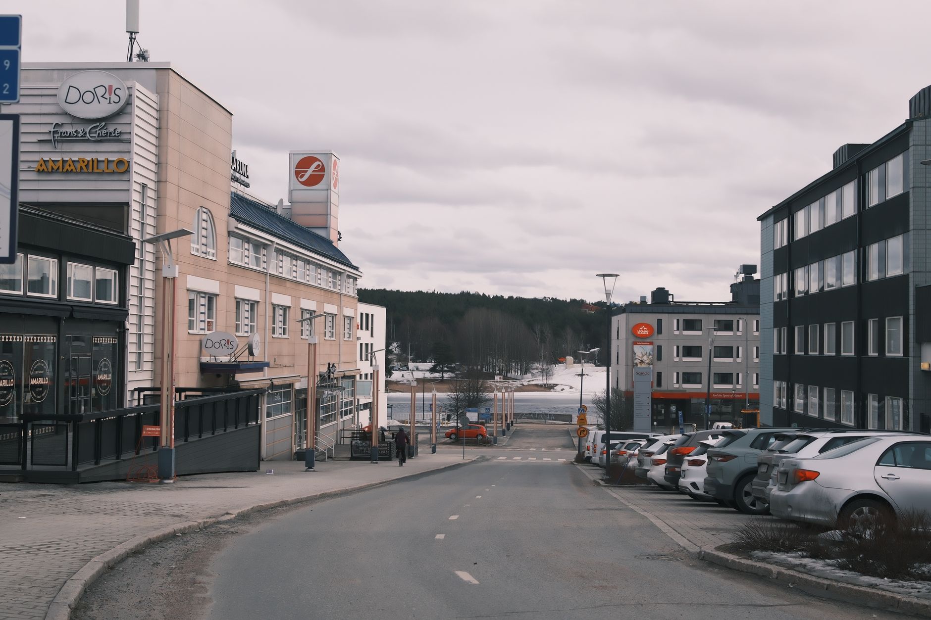 View of an urban street lined with buildings and parked cars under an overcast sky.