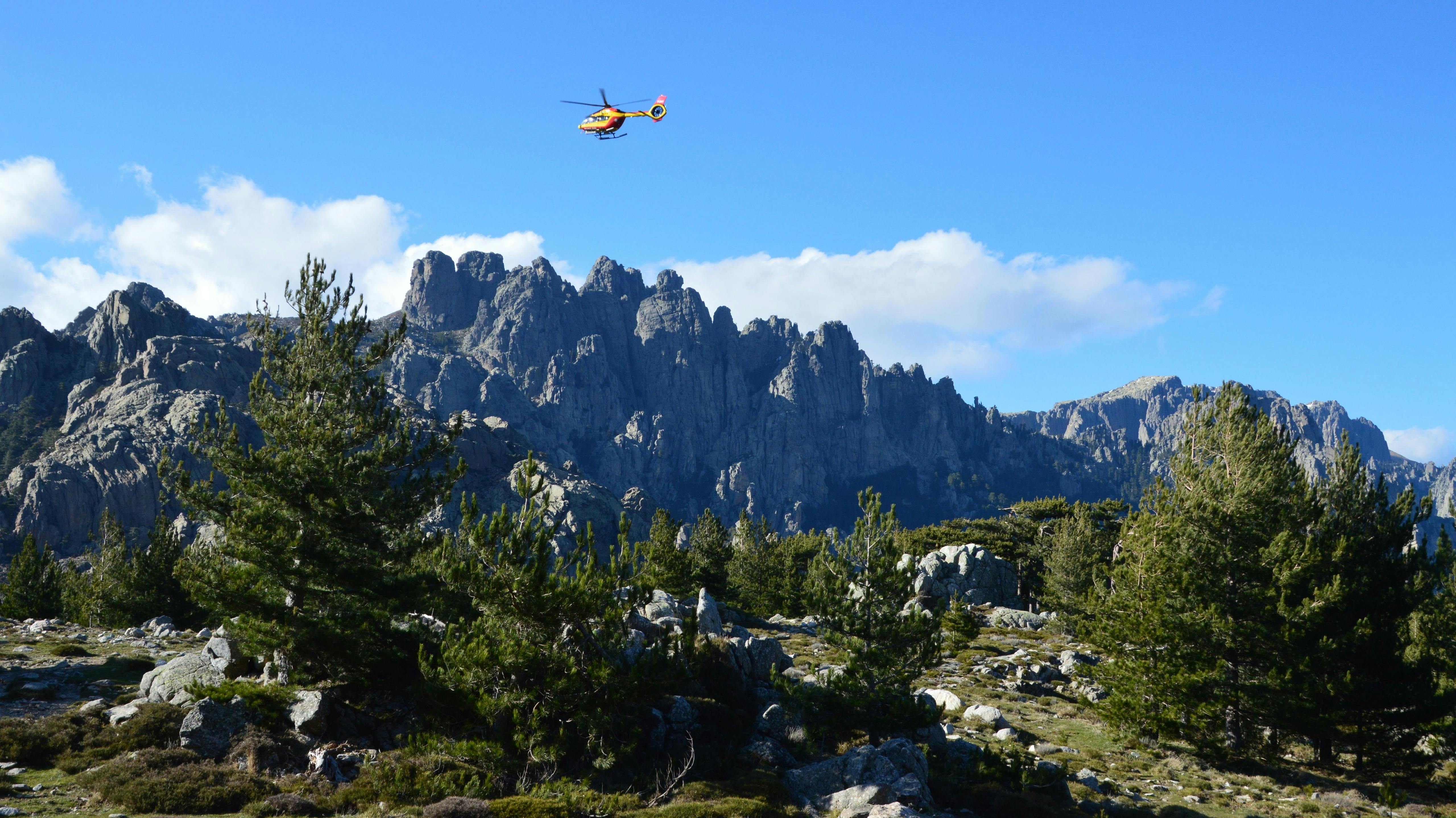 Scenic view of helicopter flying over rugged Zonza mountains and pine forest in Corsica, France.