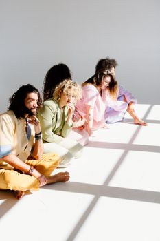 A diverse group of adults in colorful attire sit in a sunlit white studio, exuding creativity and relaxation.