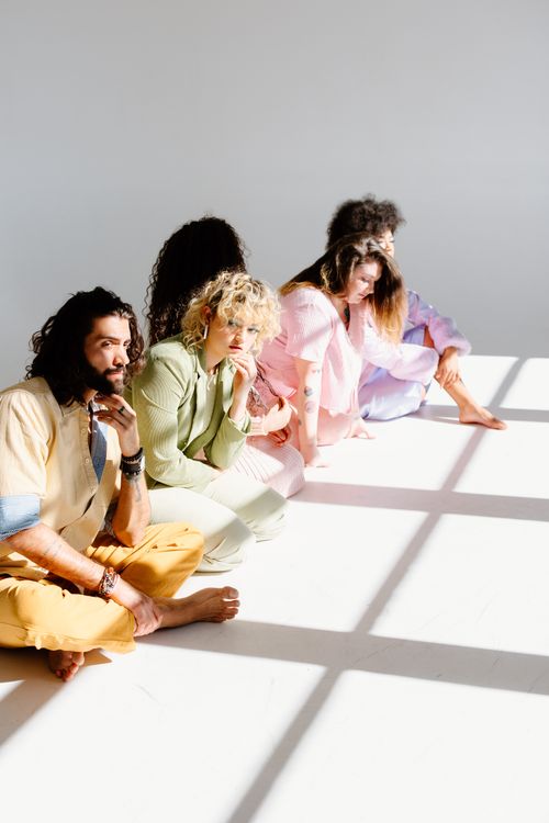 Free A diverse group of adults in colorful attire sit in a sunlit white studio, exuding creativity and relaxation. Stock Photo