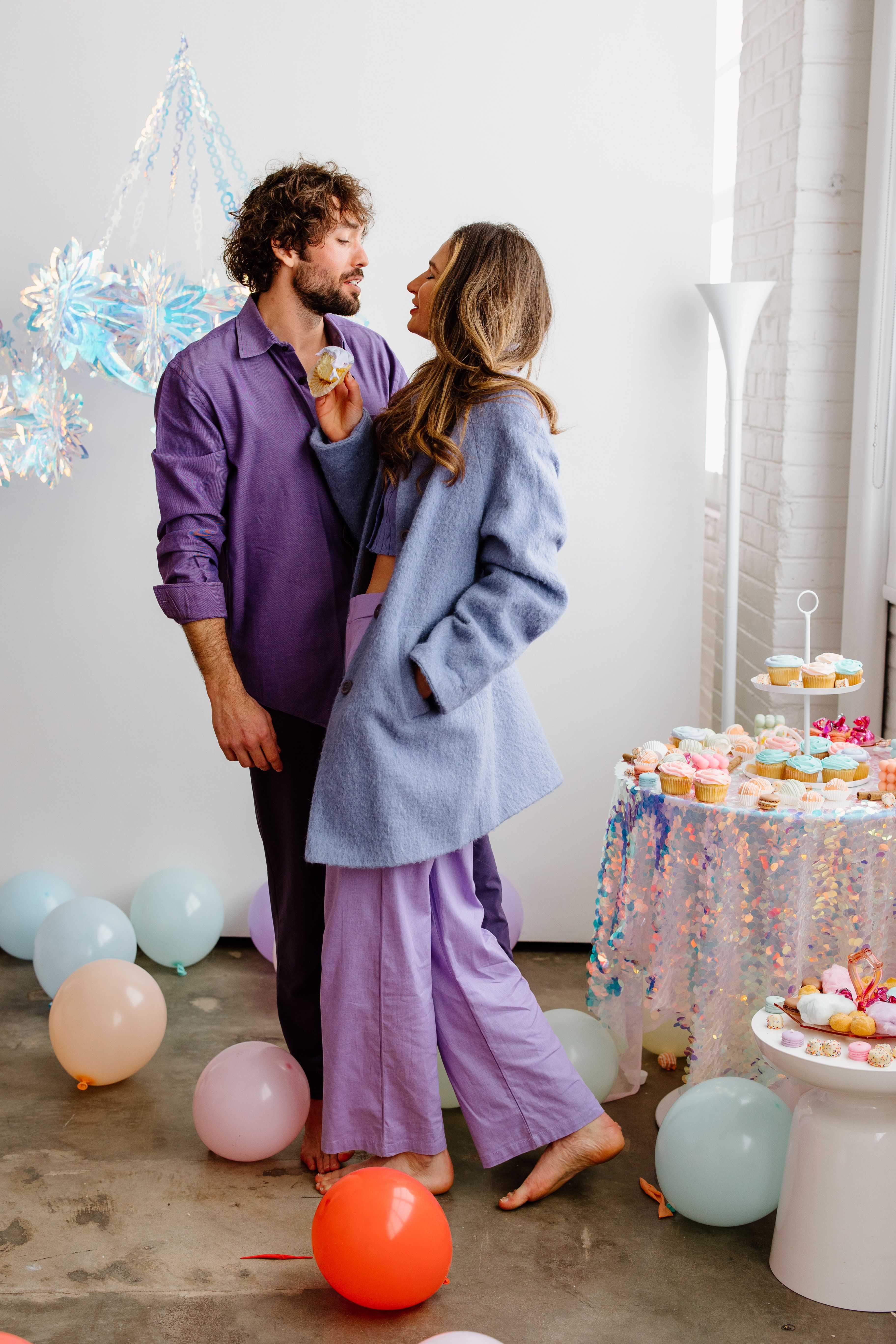 A stylish couple enjoys a festive indoor party surrounded by colorful balloons and delicious cupcakes.