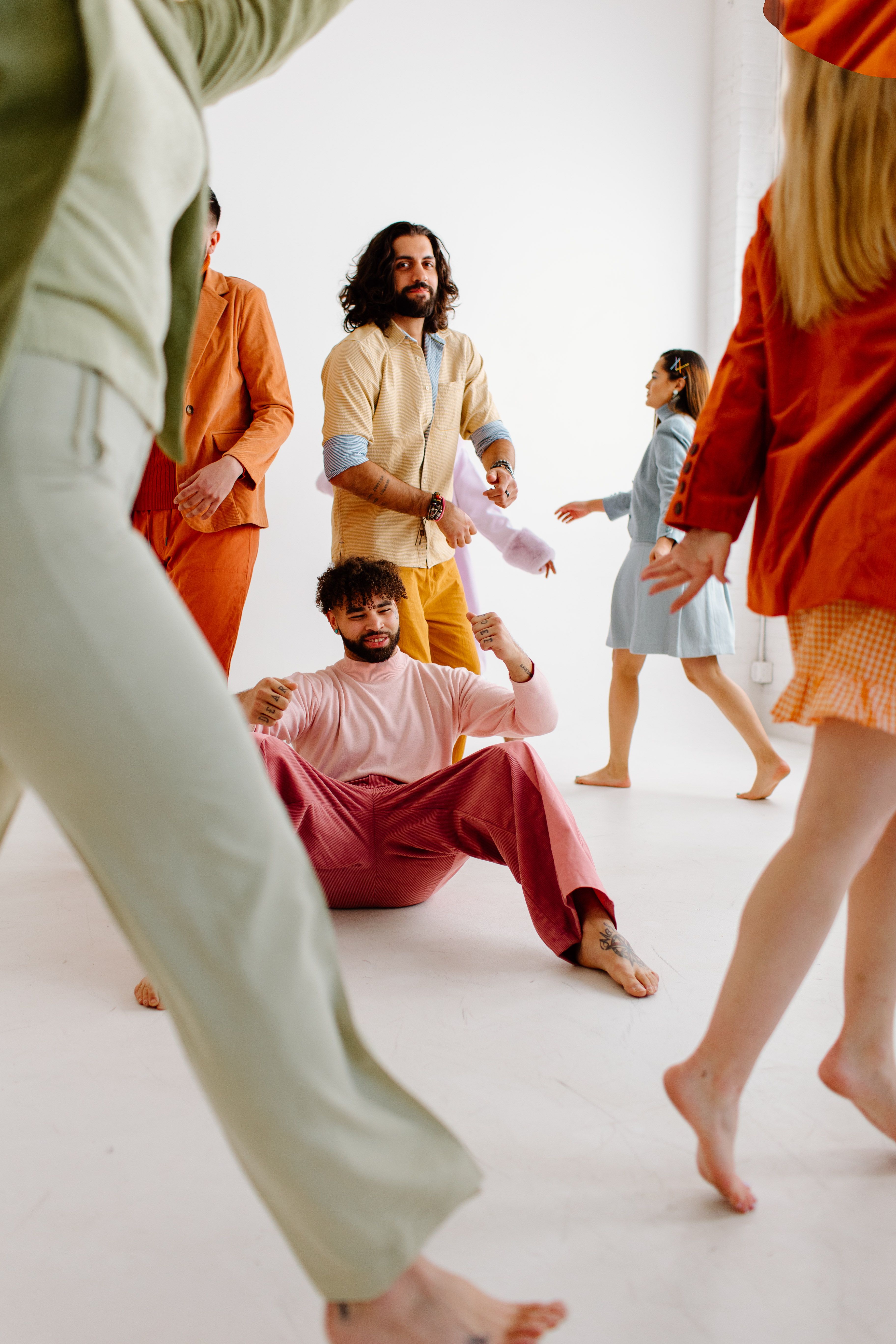 A lively group of adults dancing joyfully in a bright indoor setting wearing colorful outfits.