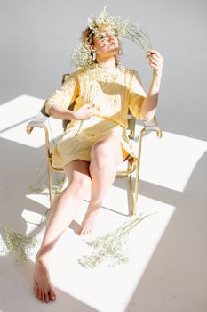 A woman in a yellow dress on a chair, adorned with baby's breath flowers in bright, natural lighting.