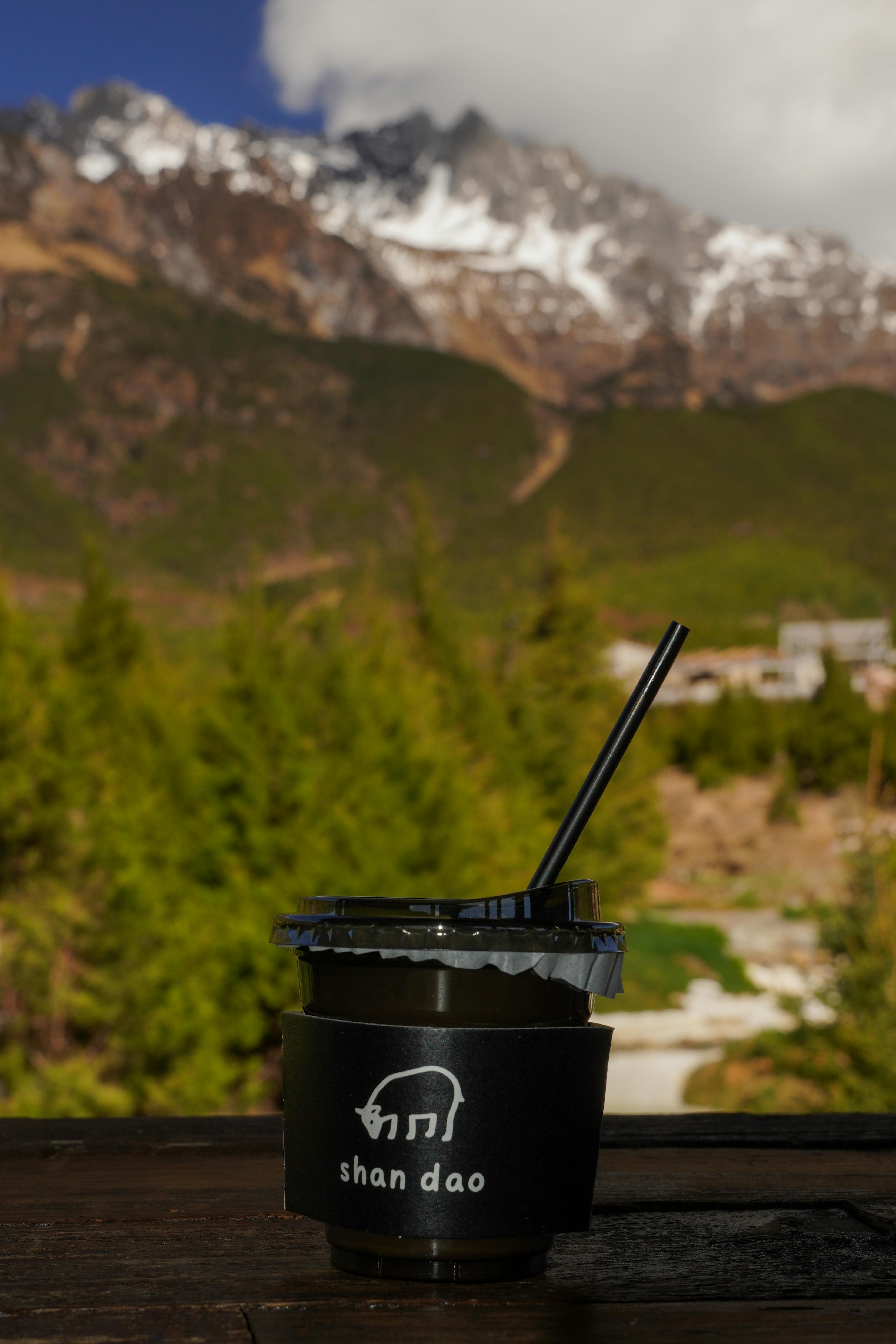 Disposable coffee cup against a stunning mountain view, ideal for travel or nature imagery.