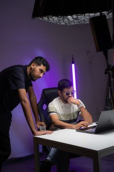 Two men in a tech-inspired workspace working on a project, illuminated by soft purple lighting.