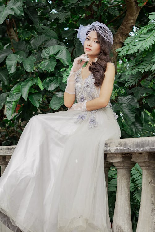 Woman in White Floral Dress Sitting on Concrete Balustrade