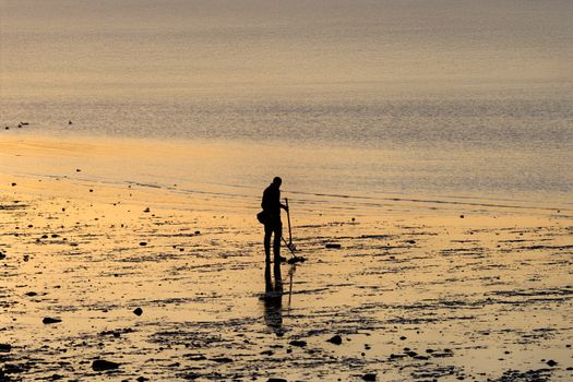 Silhouette of a person metal detecting on a tranquil beach at sunrise, Stamford, Connecticut.