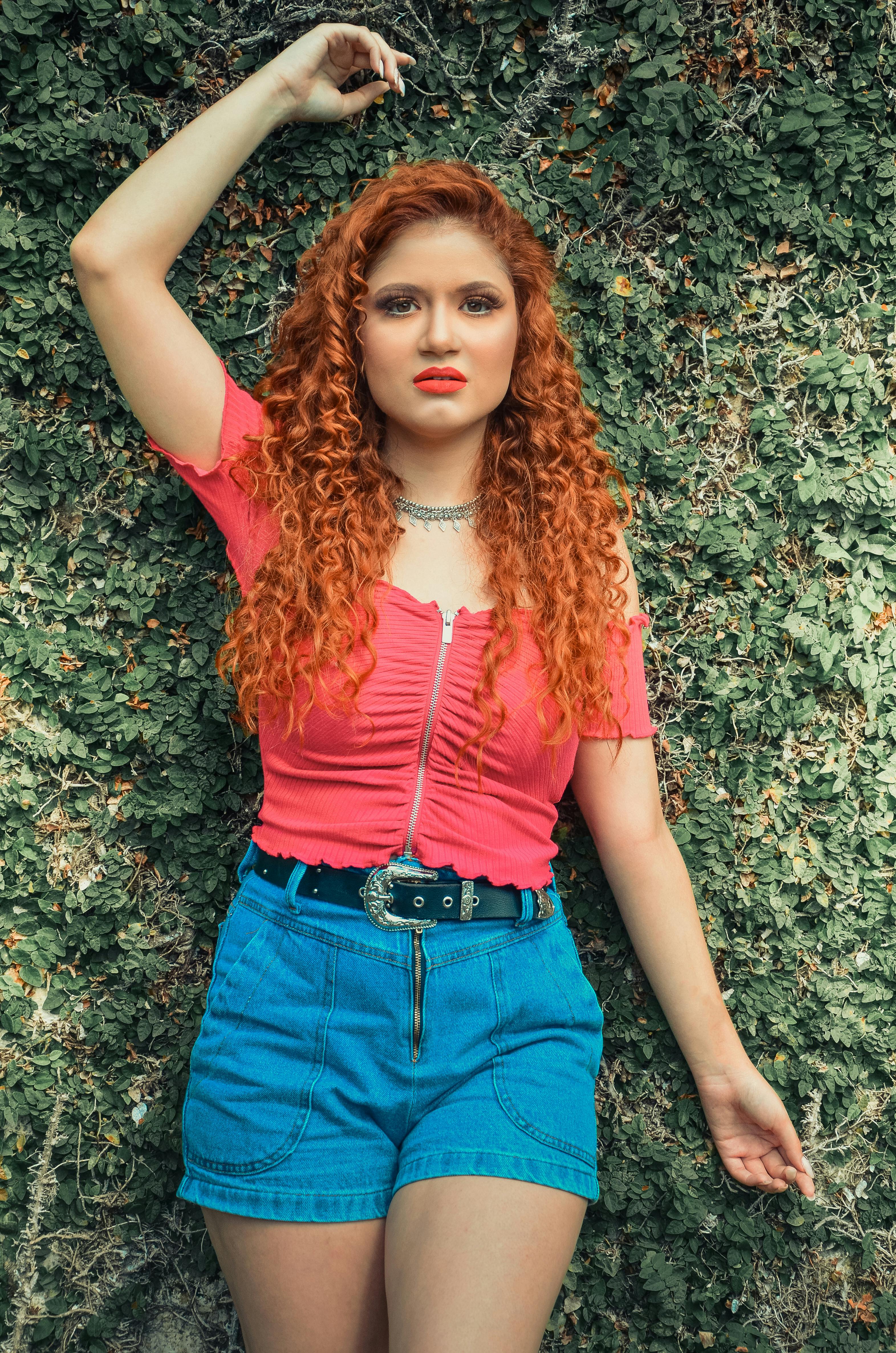 一位红发女子在郁郁葱葱的绿色背景下摆出姿势，肖像中散发着自信与时尚