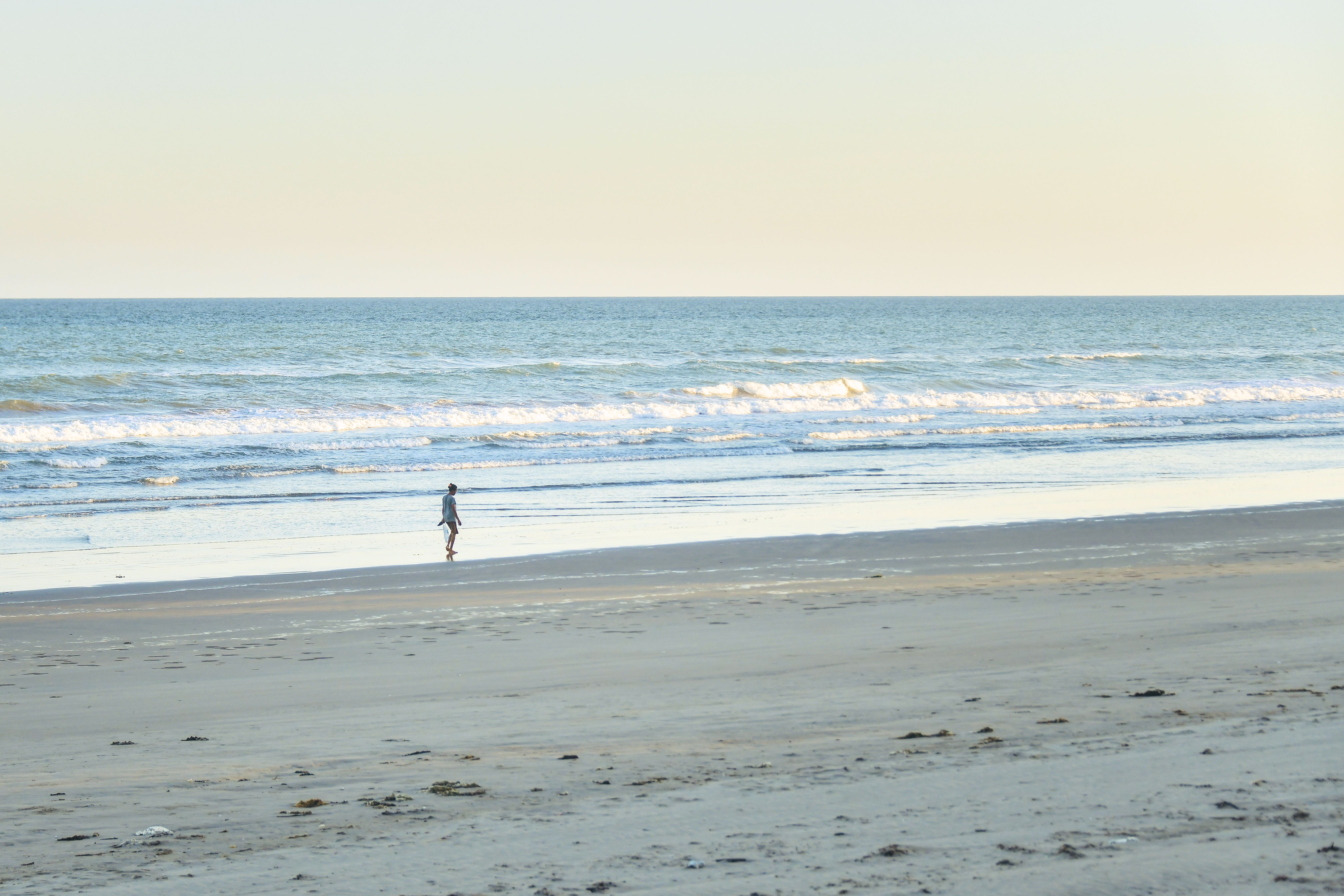 A serene beach scene in Indonesia with a lone person walking along the shore at sunrise.