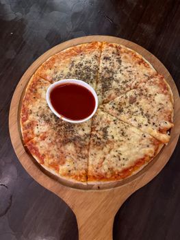 Delicious cheese pizza with herb topping and side sauce served on a wooden platter.
