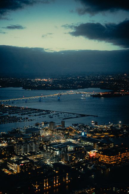 A beautiful aerial shot of a city with a bridge illuminated at twilight, showcasing urban lights and water reflections.
