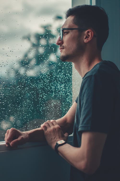 Free Man Leaning On Glass Window Watching The Rain Stock Photo