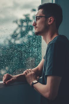 一个戴眼镜的年轻人若有所思地望着室内的雨窗