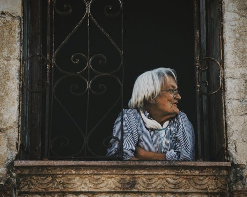Free Portrait of a senior woman gazing outward from an old, rustic window. Stock Photo
