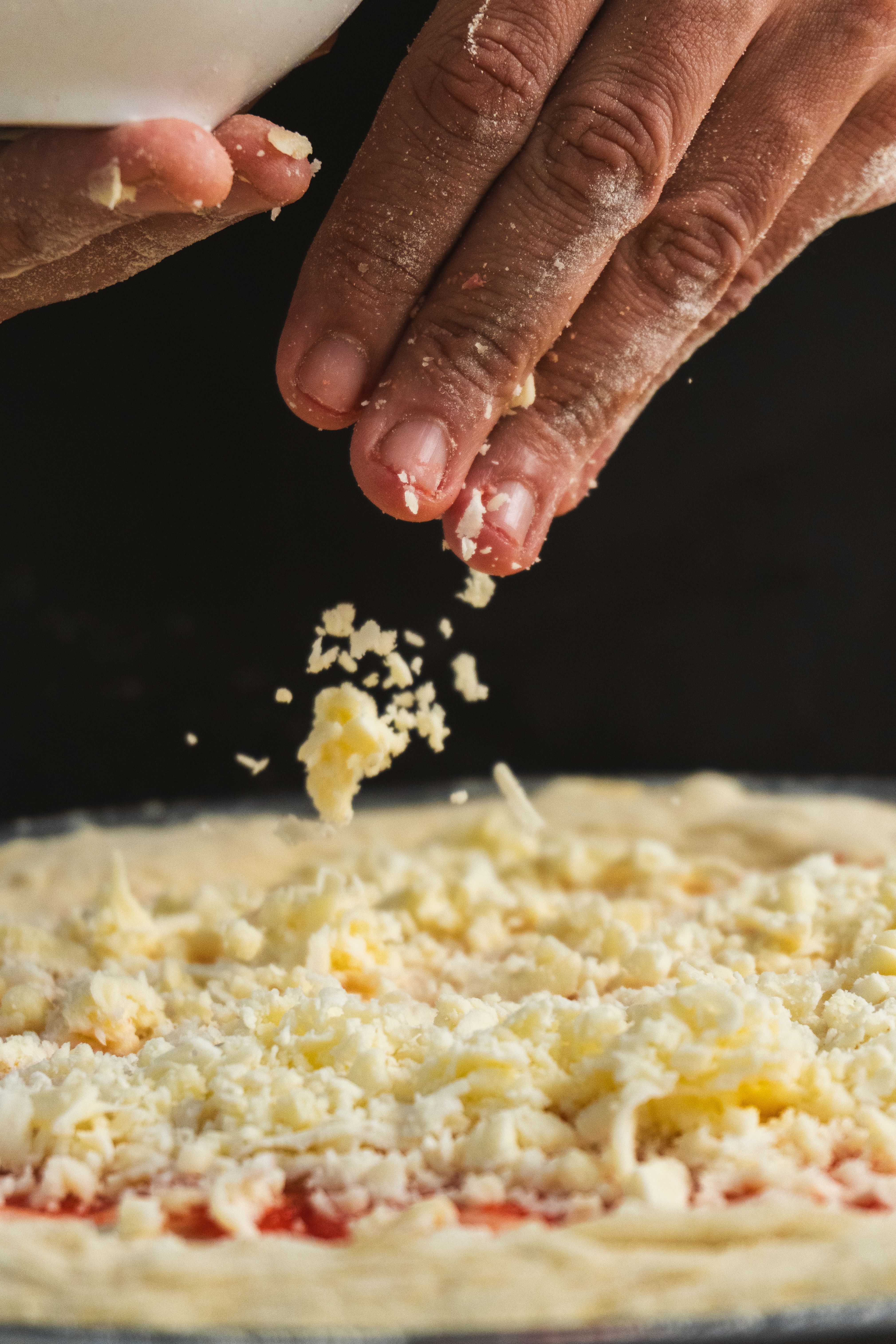 Preparing pizza with grated cheese being sprinkled onto dough. A close-up, culinary action shot for food enthusiasts.