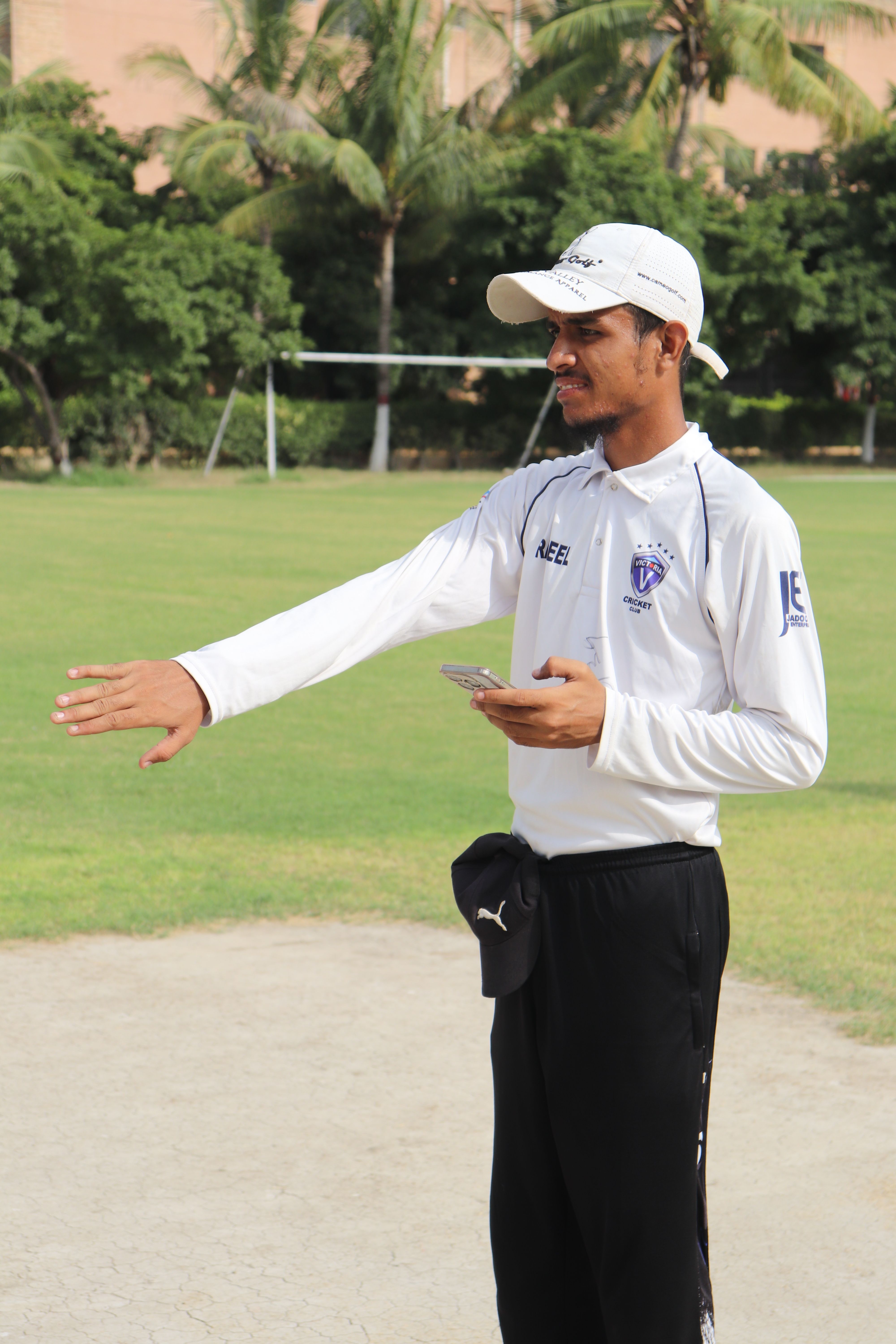 A cricket coach in white uniform instructing a player on a sunny day at the cricket ground.