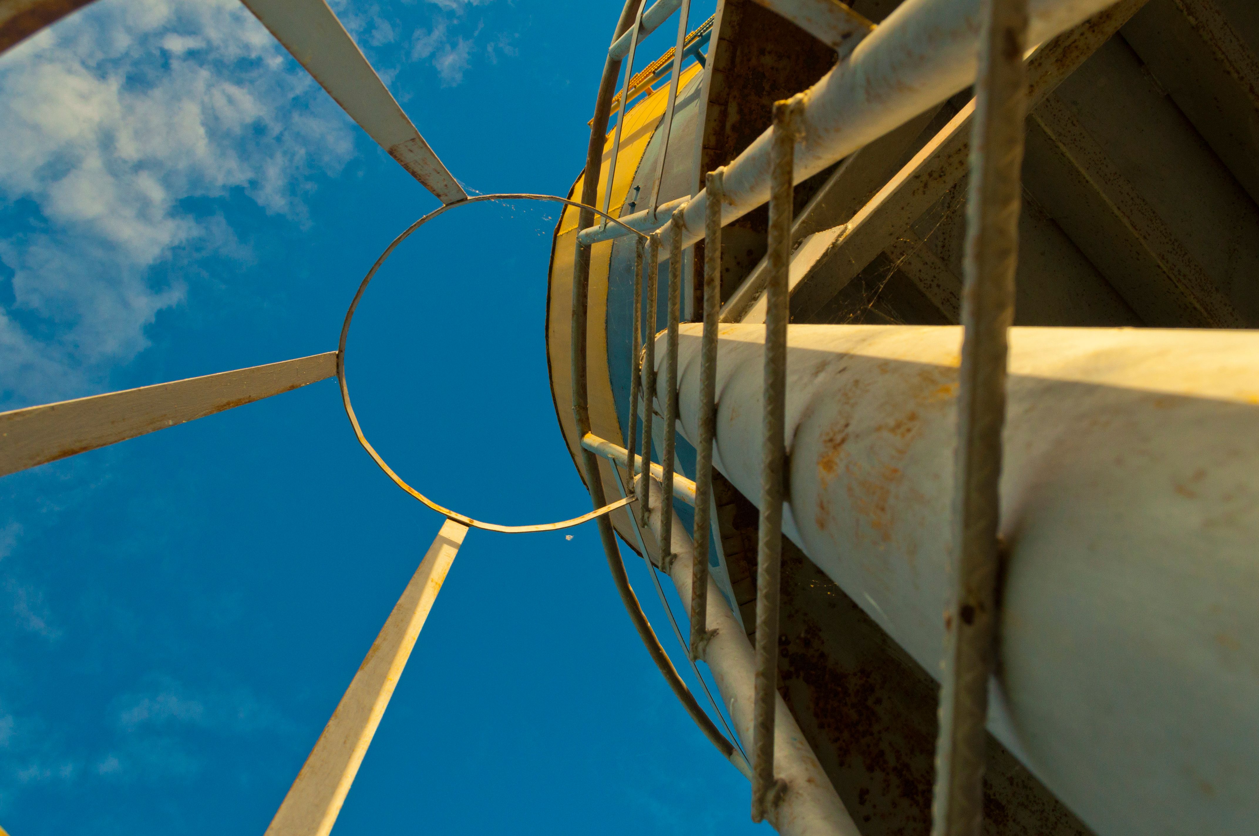 Looking up at an industrial metal structure with blue sky and clouds above.