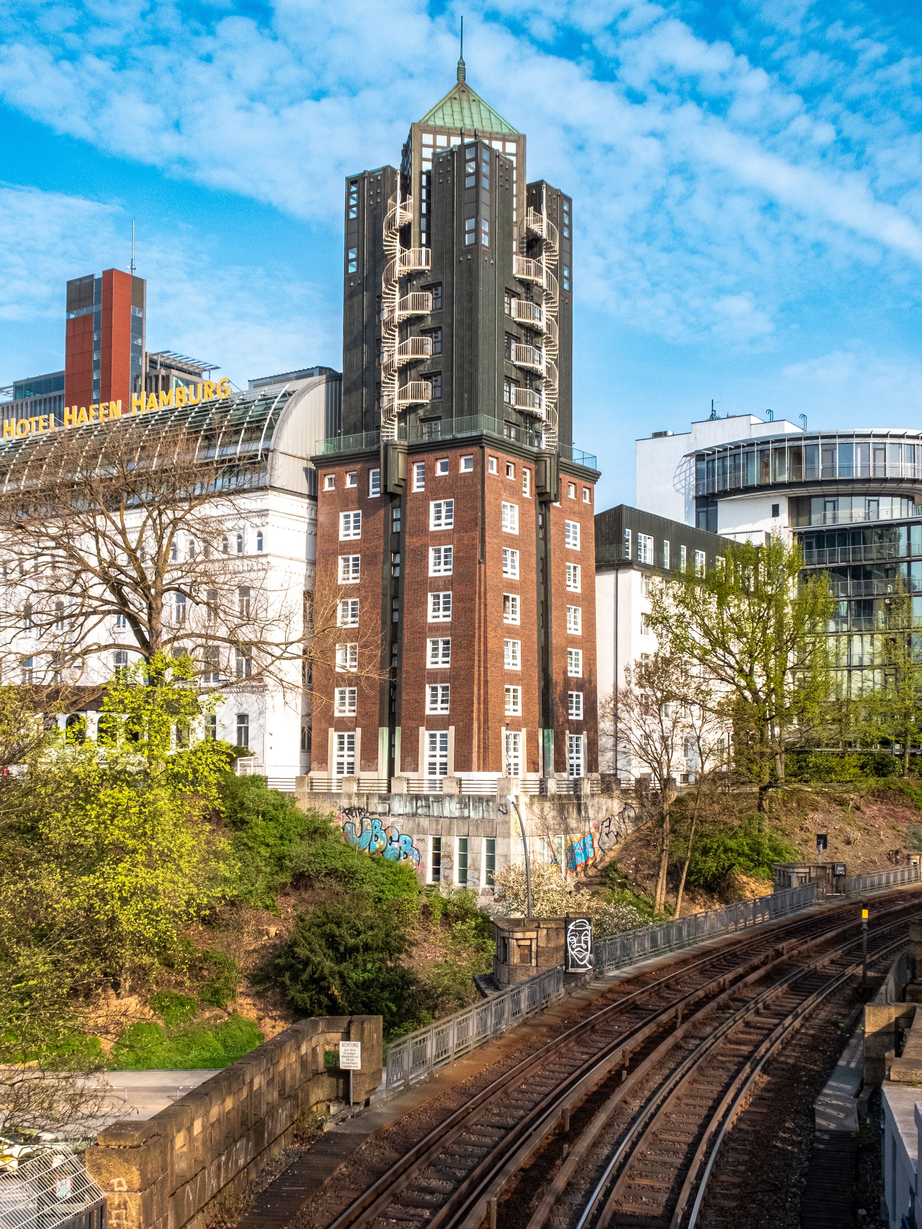 A modern tower in Hamburg, Germany, stands tall beside railway tracks on a clear day.