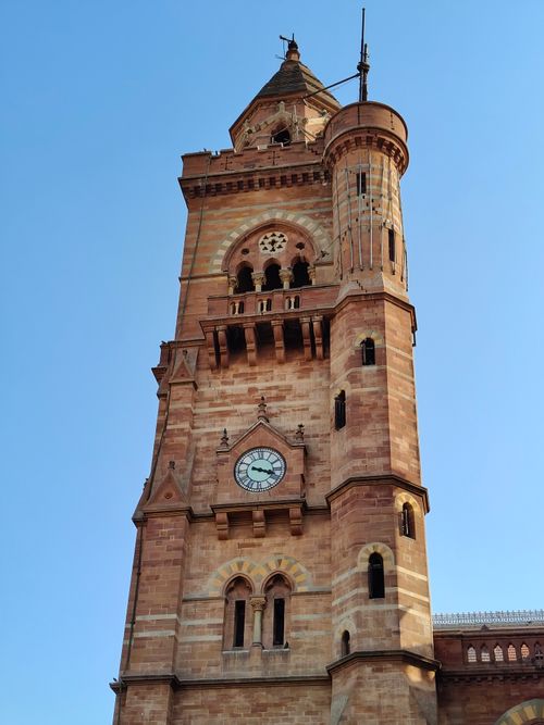 Free A majestic historic clock tower stands tall against a clear blue sky, showcasing intricate architecture. Stock Photo