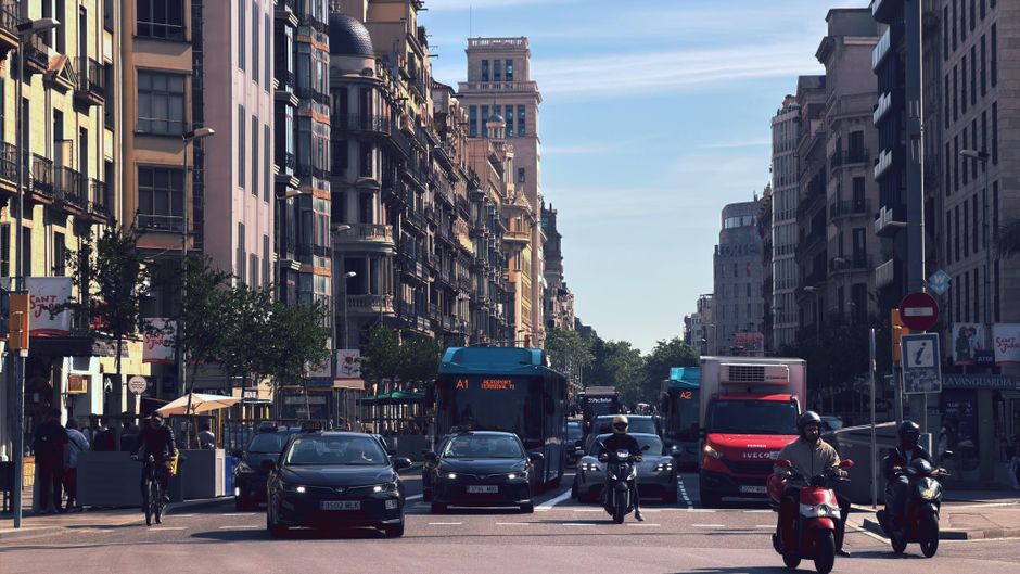 Vista de una calle concurrida en el centro de Barcelona, con coches, autobuses y motocicletas frente a una arquitectura emblemática.