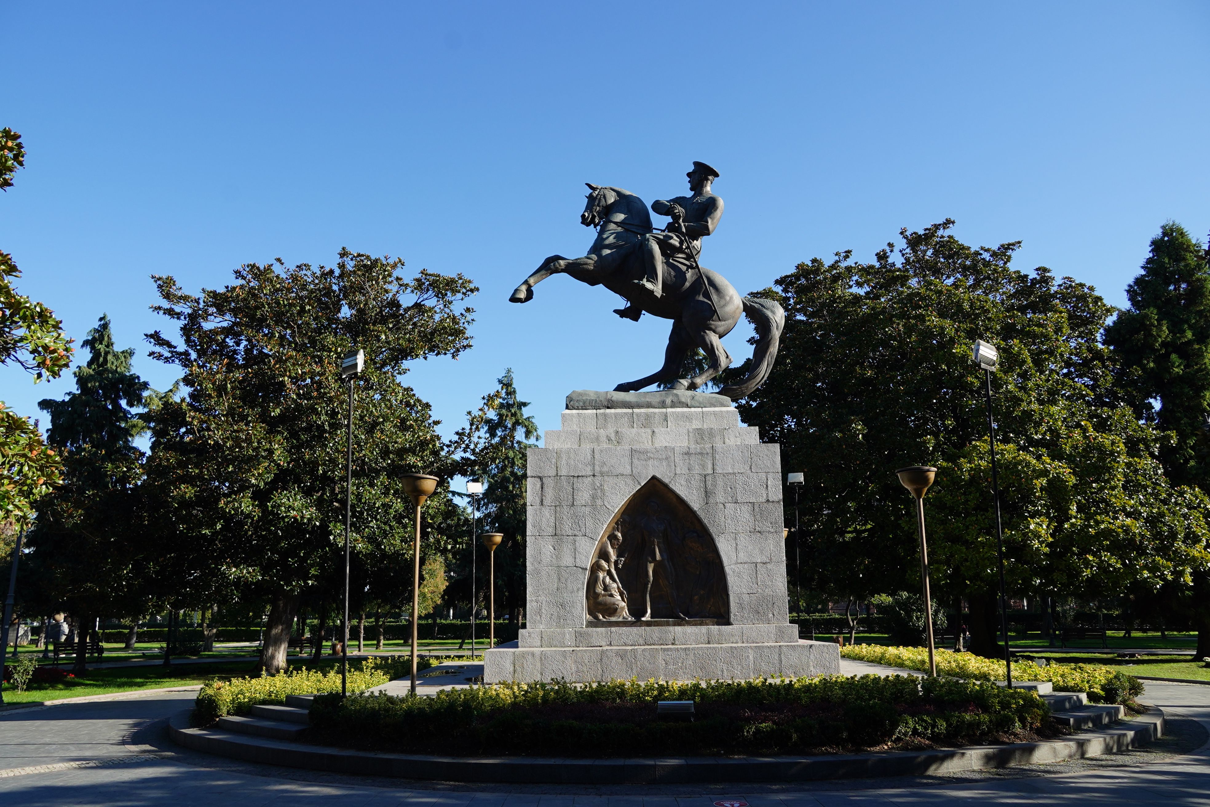 A majestic equestrian statue in a sunny park surrounded by lush greenery.