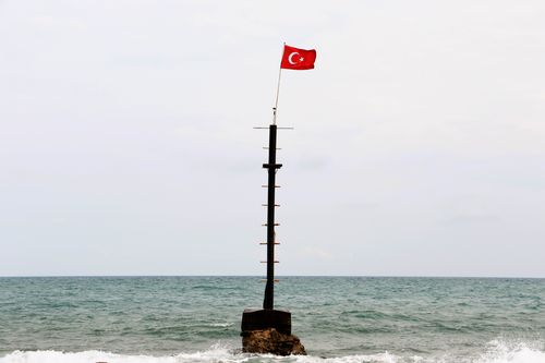 Free Turkish flag fluttering on isolated seaside mast against a calm sea backdrop. Stock Photo