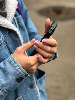 一名女子手持智能手机，指甲修剪整齐，穿着牛仔夹克的近景特写